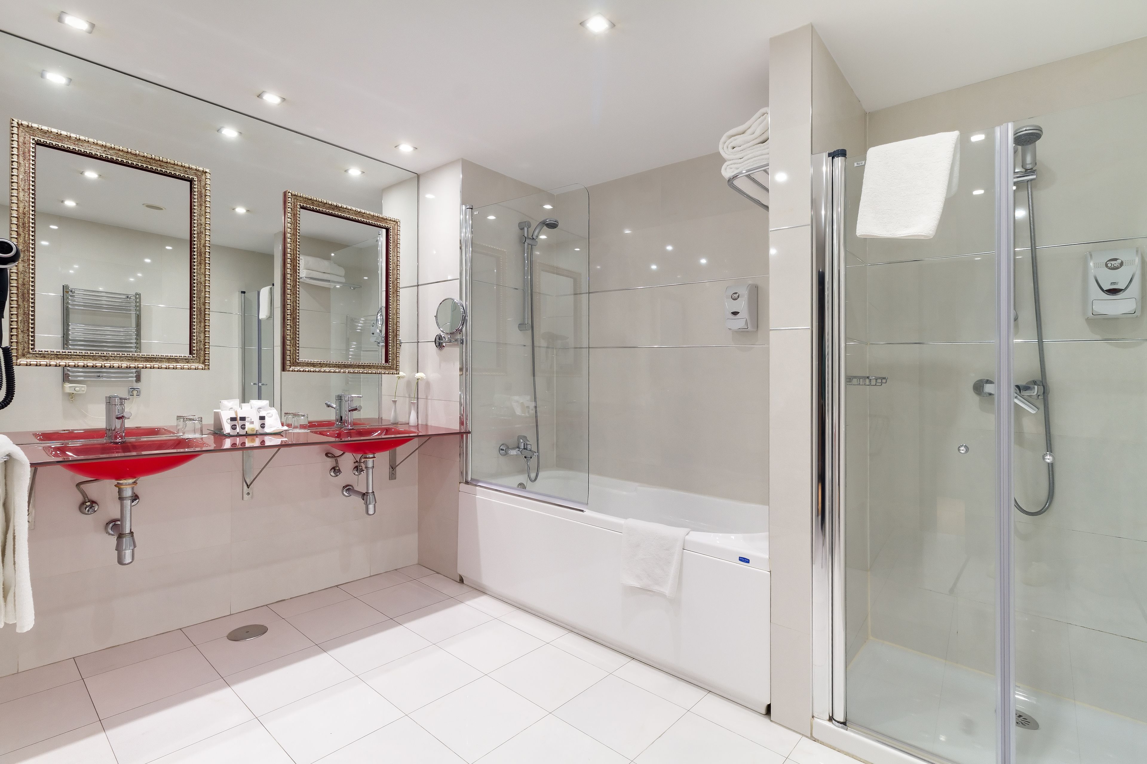 A modern bathroom with a glass-enclosed shower, a white bathtub, and two red sinks with mirrors.
