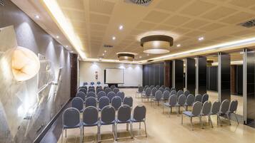 A conference room with rows of chairs, a podium, and a large screen.