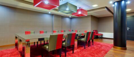 A conference room with a glass table, red and grey chairs, and red pendant lights.