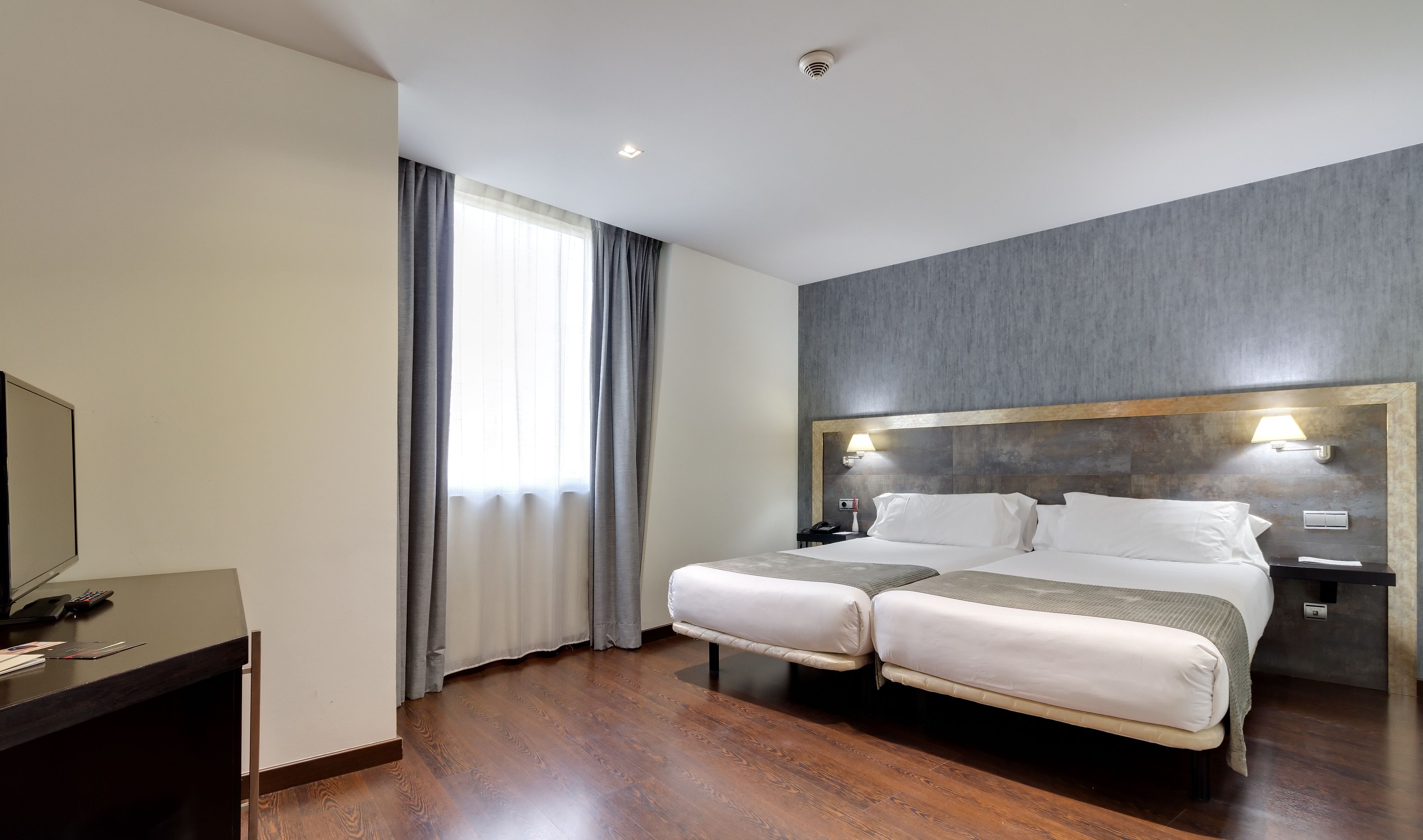A hotel room with a large bed, a desk with a computer, and a window with curtains.