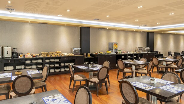 Ein Hotel-Speisesaal mit mehreren Tischen und Stühlen, einer Buffetstation mit verschiedenen Speisen und einer Kaffeestation.