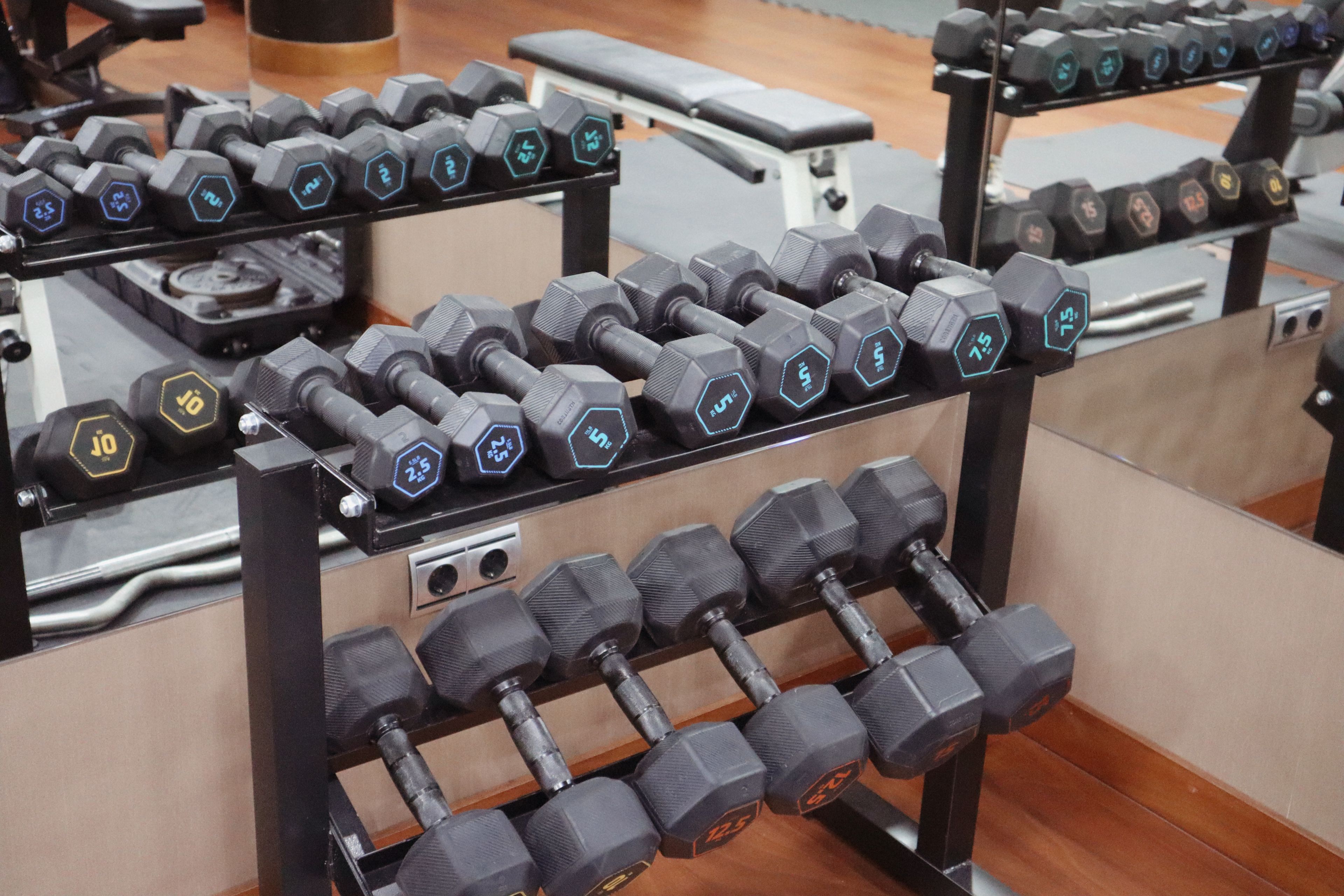 Un estante con mancuernas de diferentes pesos, dispuesto en el suelo de un gimnasio.