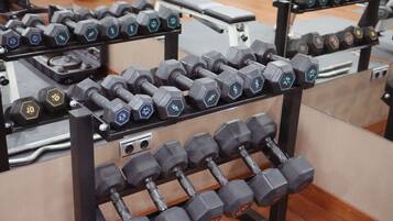 Un estante con mancuernas de diferentes pesos, dispuesto en el suelo de un gimnasio.