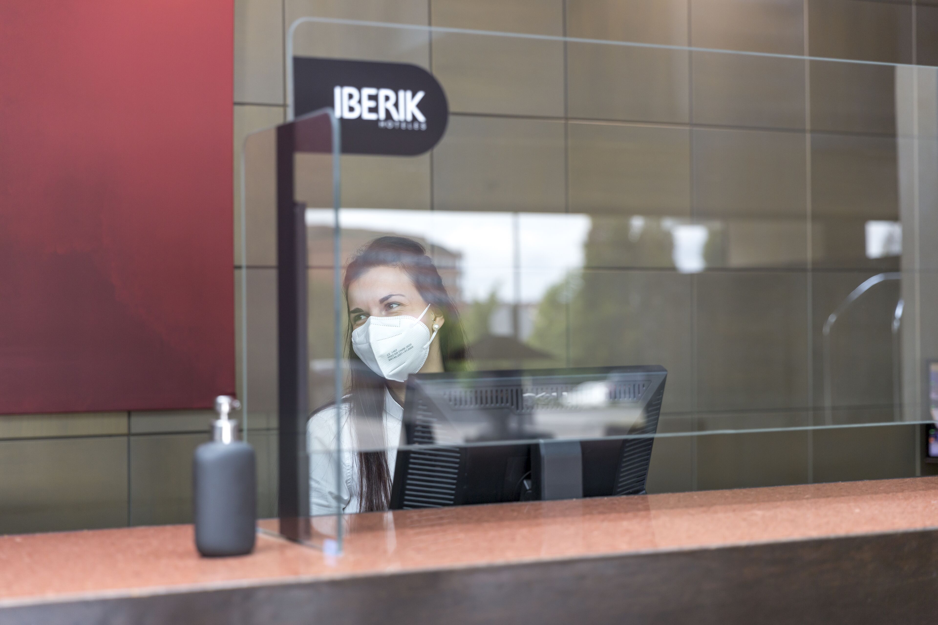 A reception desk with a sign that reads "IBERIK HOTELS" and a bottle of hand sanitizer on the counter.