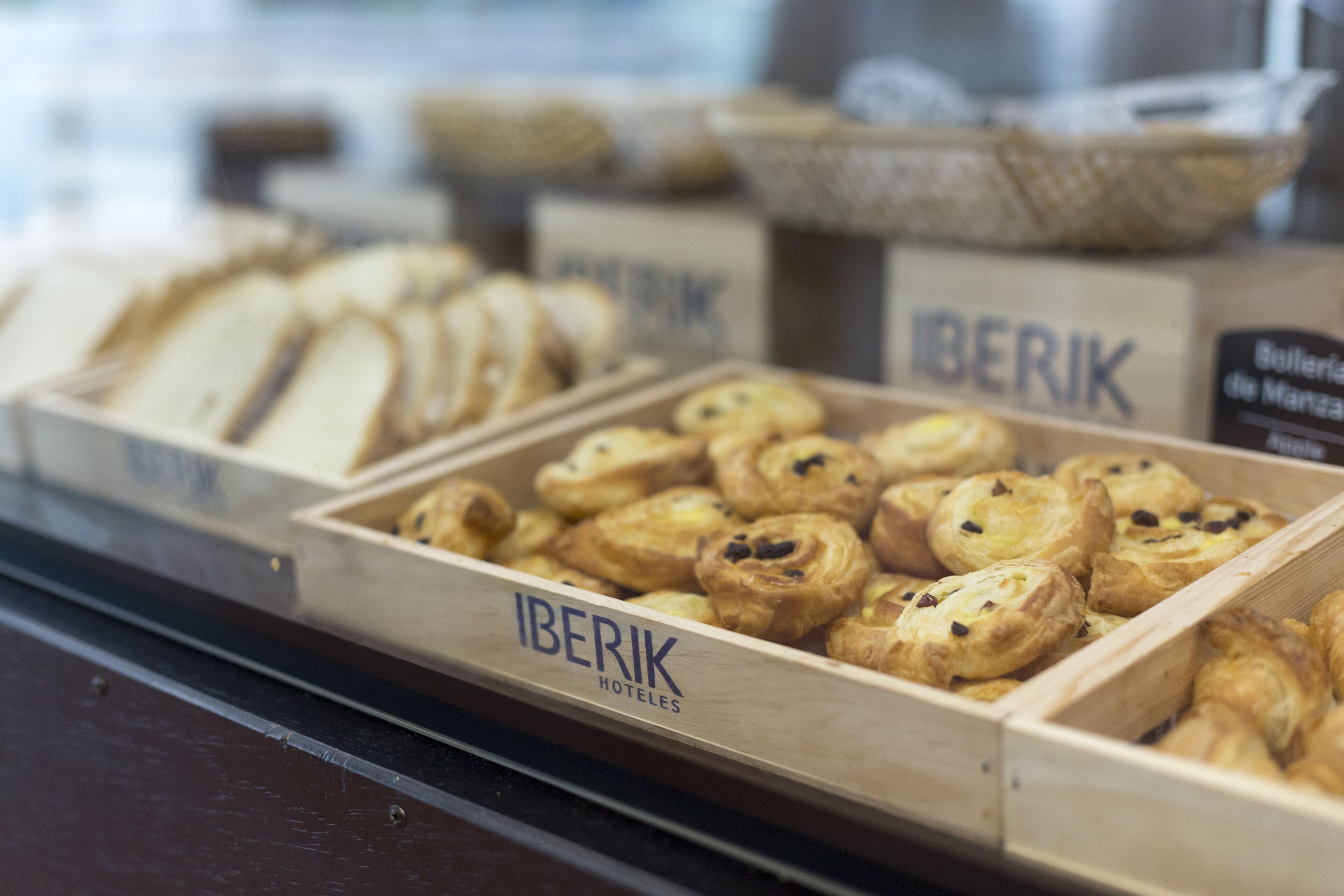 Exposição de doces em caixas de madeira com a inscrição 'IBERIK HOTELES'.