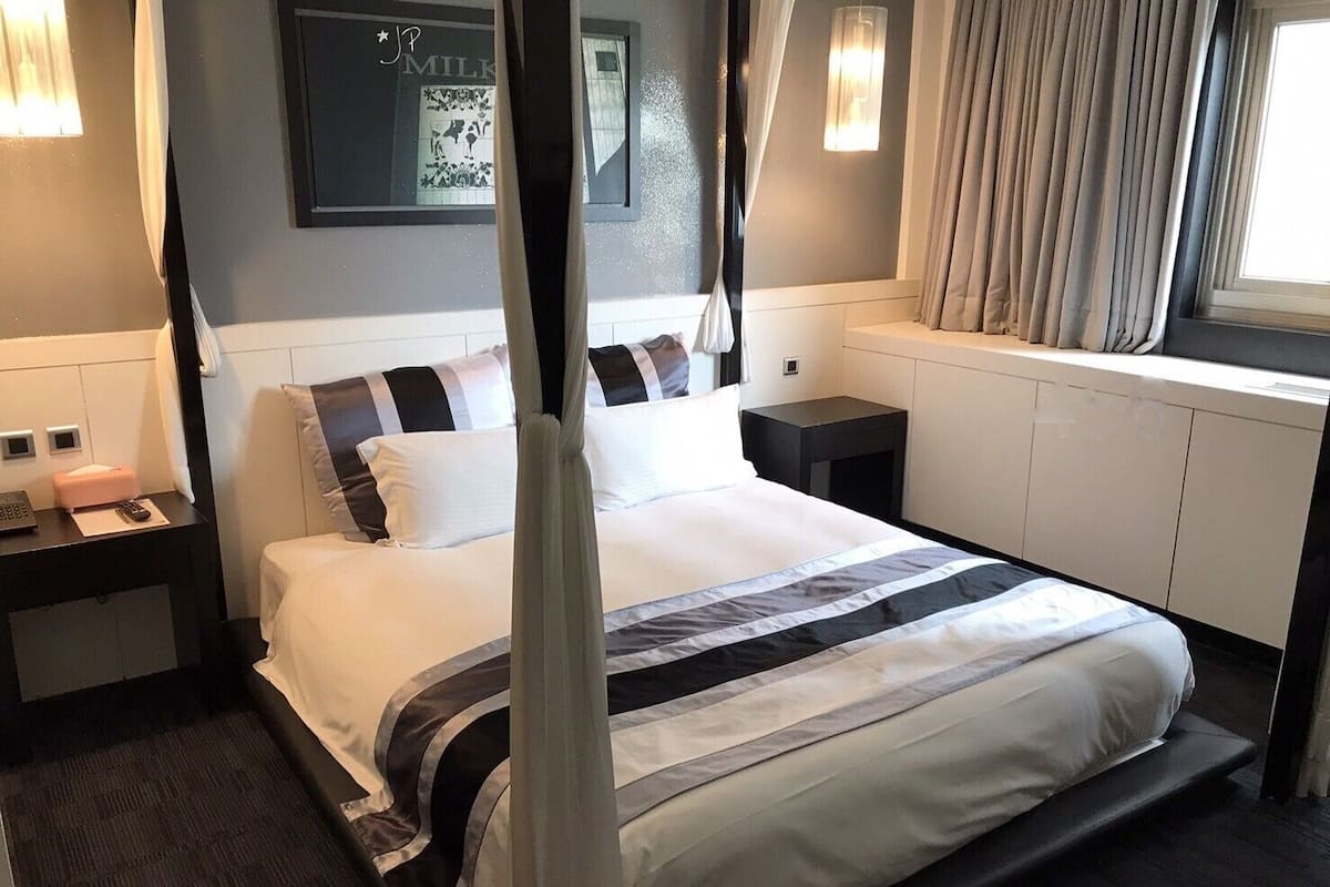 Una camera d'albergo moderna con un letto grande, un comodino, tende e un punto luce a parete.