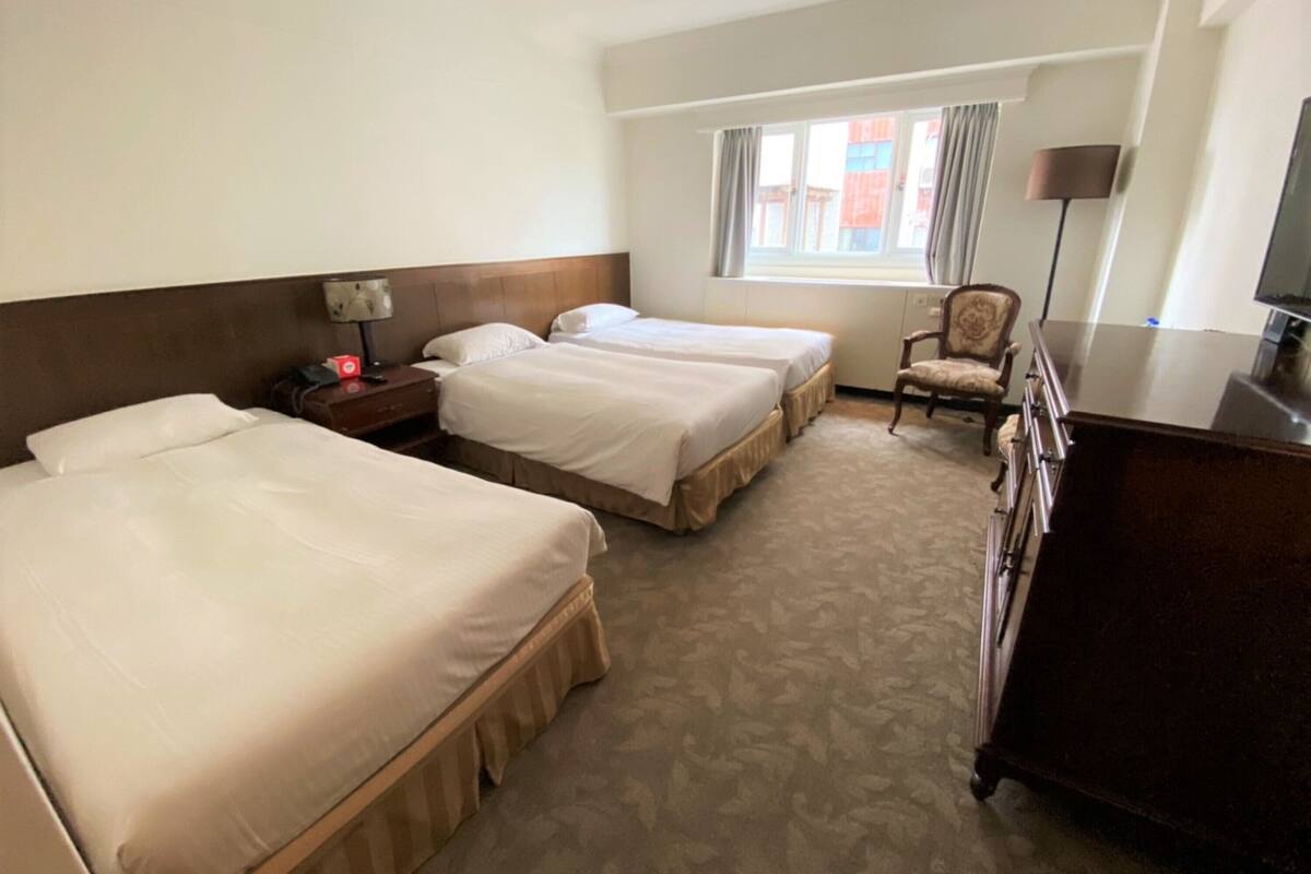 Una camera d'albergo con due letti, una scrivania, una sedia, una televisione e una finestra con tende.