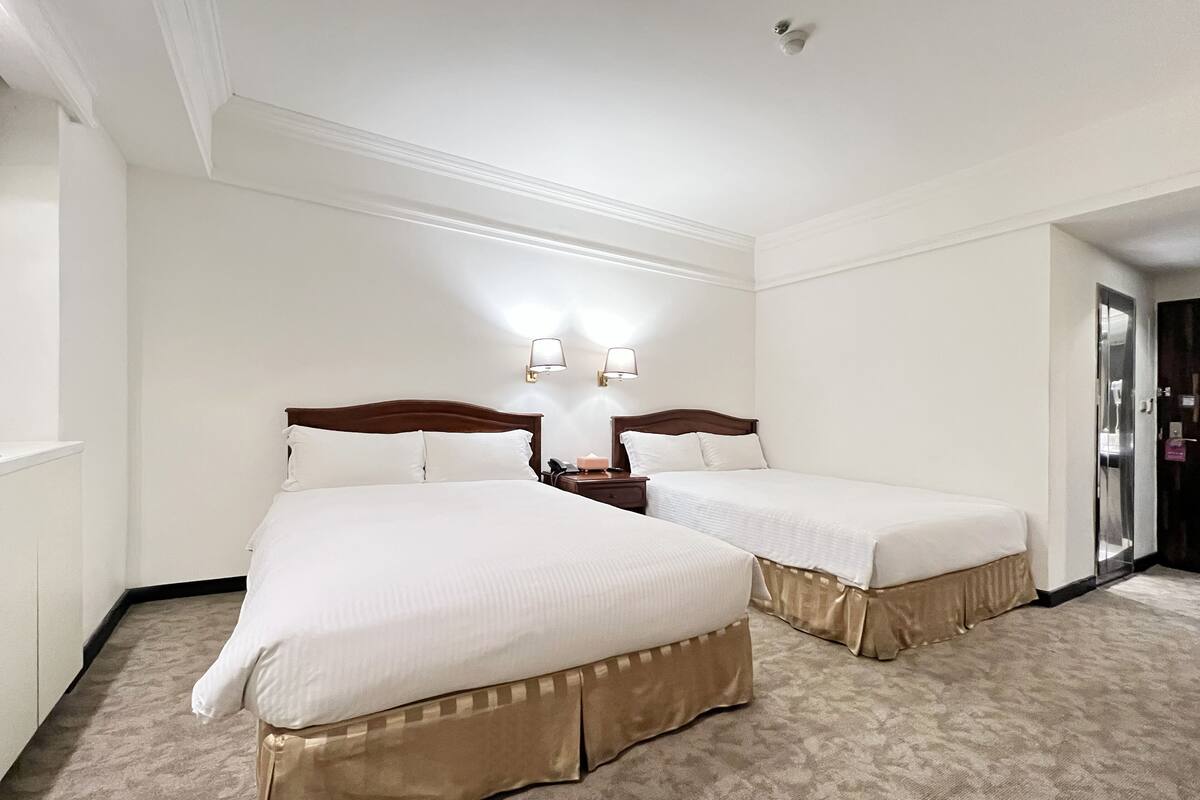 Una camera d'albergo con due letti, un comodino e una lampada fissata al muro.