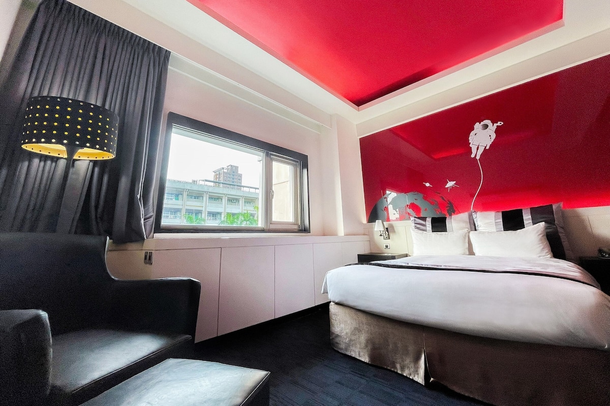 Una camera d'albergo con un letto, una scrivania, una sedia, una finestra e una parete decorata di rosso.