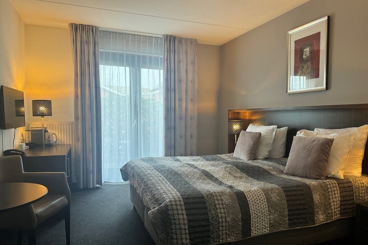 A hotel room with a large bed, a desk with a chair, a television, and a framed picture on the wall.