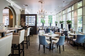 A spacious restaurant with high ceilings, large windows, and a chandelier. Tables and chairs are arranged for dining. - Hampshire Avenarius (Ruurlo)
