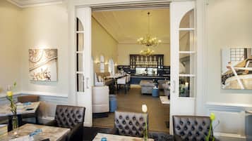 Un hall de hotel con zona de comedor, asientos, bar y una araña.