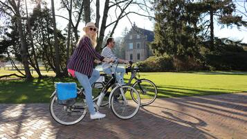 Two people riding bicycles on a paved path with a grassy area and trees in the background.