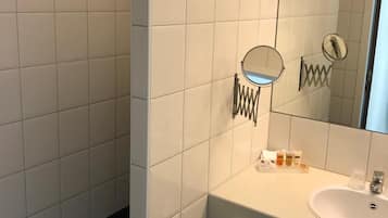 A bathroom with white tiles, a sink, a mirror, and toiletries.