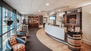 Uma área de recepção com assentos de couro, um barril de madeira e uma tela de TV.