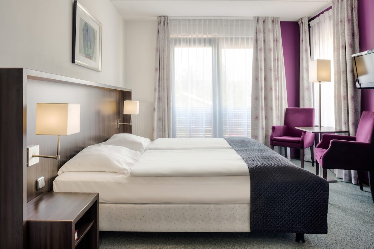 A hotel room with a double bed, two bedside tables, a desk, a chair, a TV, and a window with curtains.