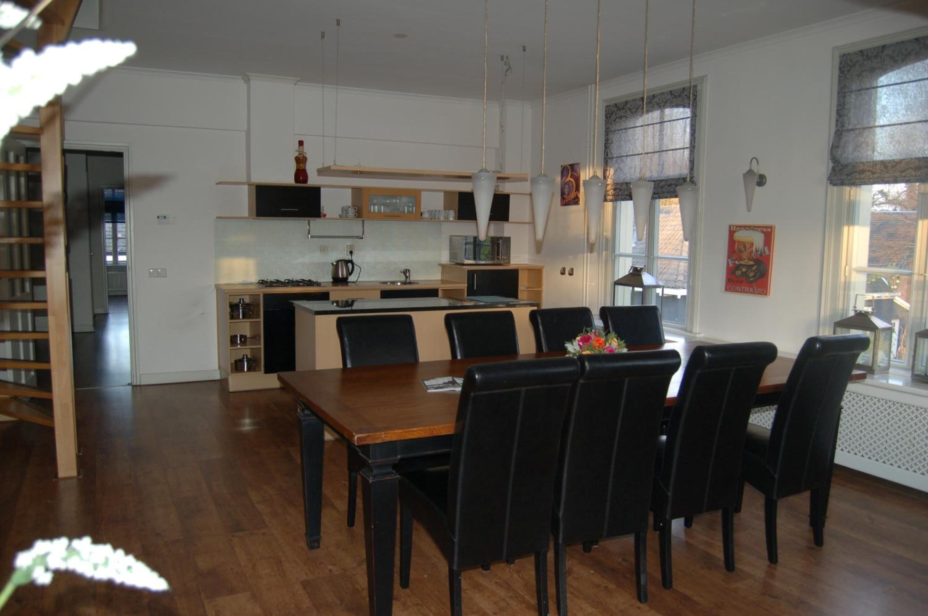 Une cuisine moderne avec des meubles blancs, un îlot central et des chaises noires disposées autour d’une table à manger en bois.
