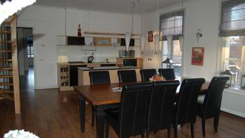 Une cuisine moderne avec des meubles blancs, un îlot central et des chaises noires disposées autour d’une table à manger en bois.
