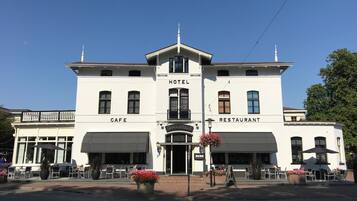 Un bâtiment blanc avec une entrée centrale, portant les indications « hôtel », « café » et « restaurant ».
