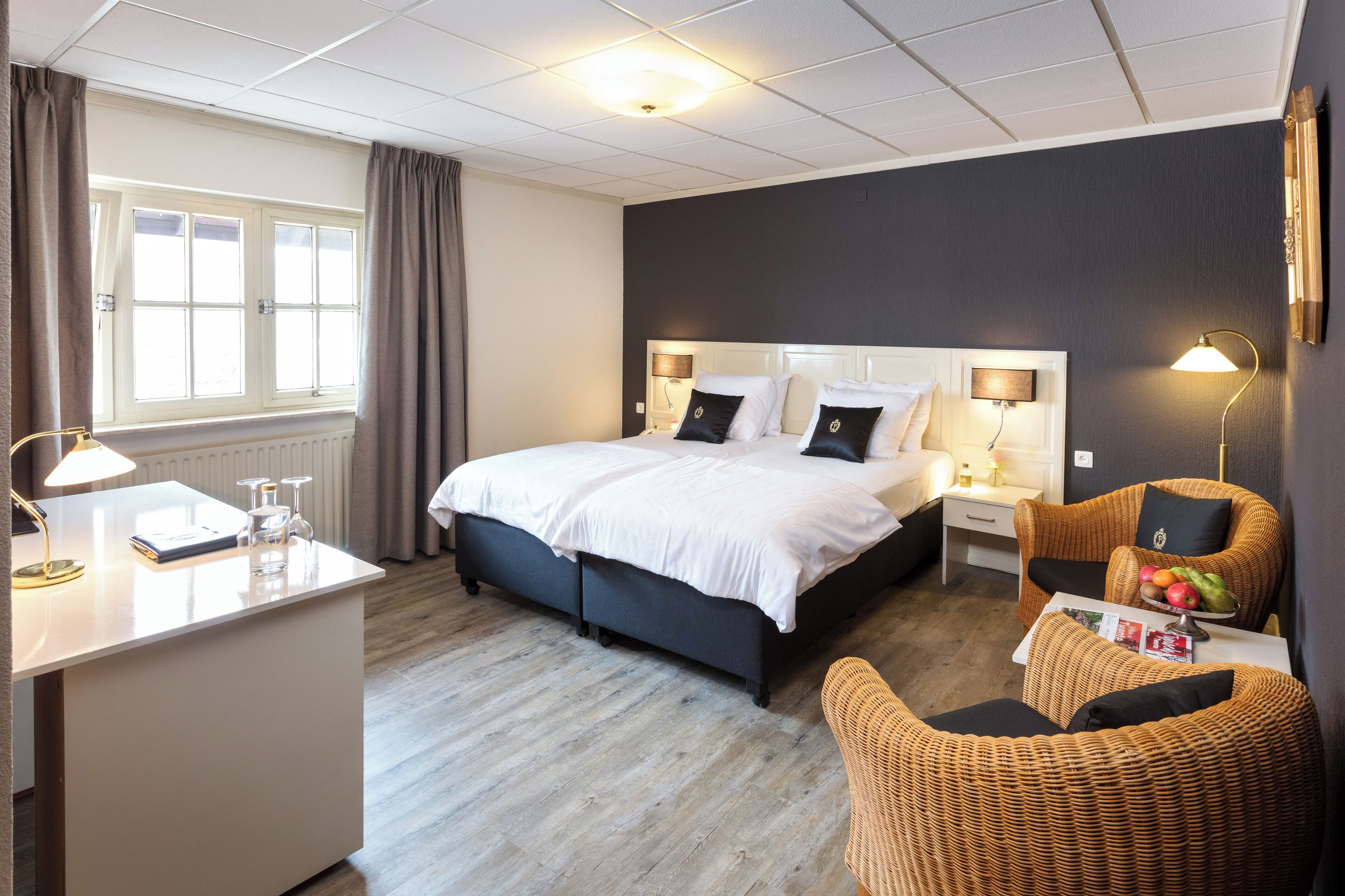 A hotel room with a bed, bedside tables, a desk, a chair, and a window.