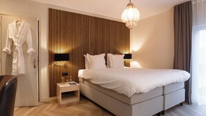 Moderni hotellihuone, jossa on suuri sänky, yöpöytä, ovenkahvassa roikkuva kylpytakki ja puupaneloitu seinä.