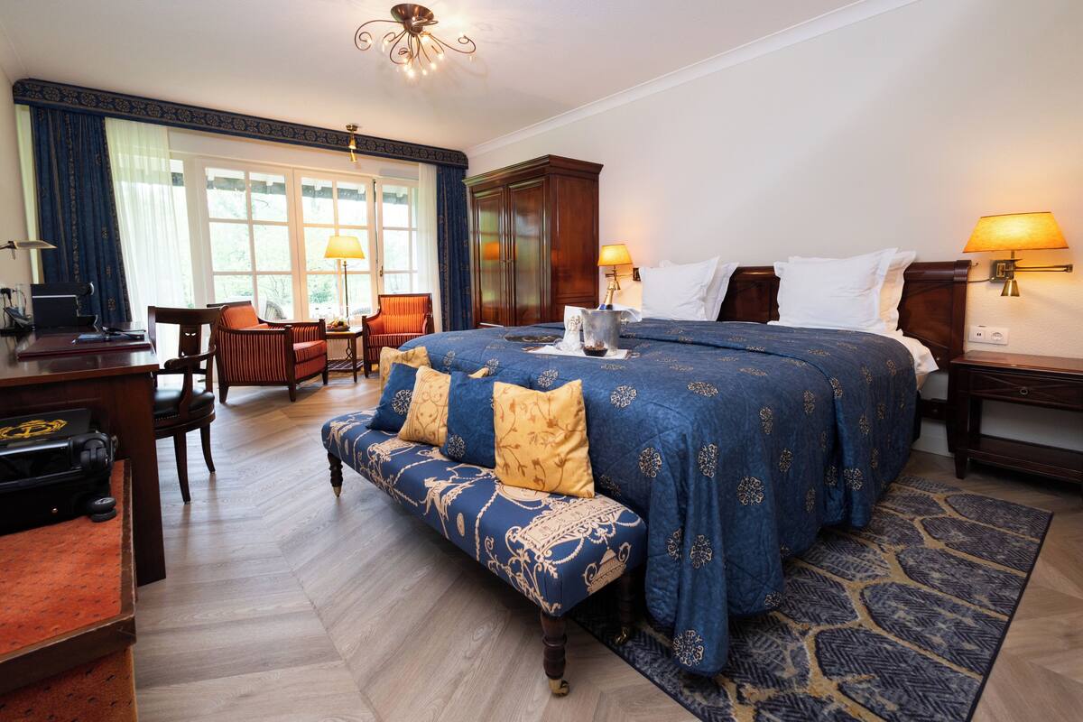A hotel room with a large bed, a bench, a desk with a computer, and a wardrobe.