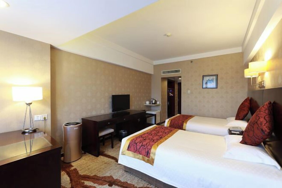 A hotel room with two beds, a desk, a television, and a trash can.