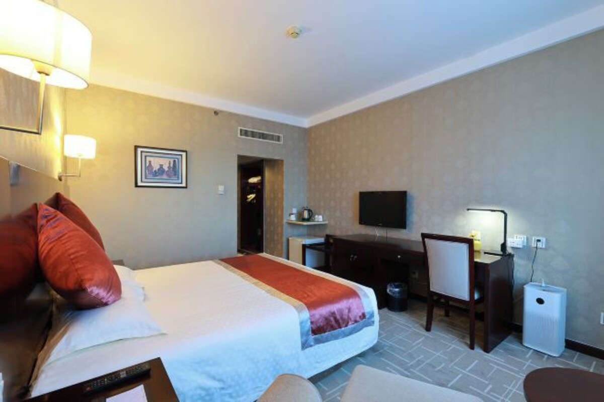 A hotel room with a bed, desk, chair, TV, and a small table.
