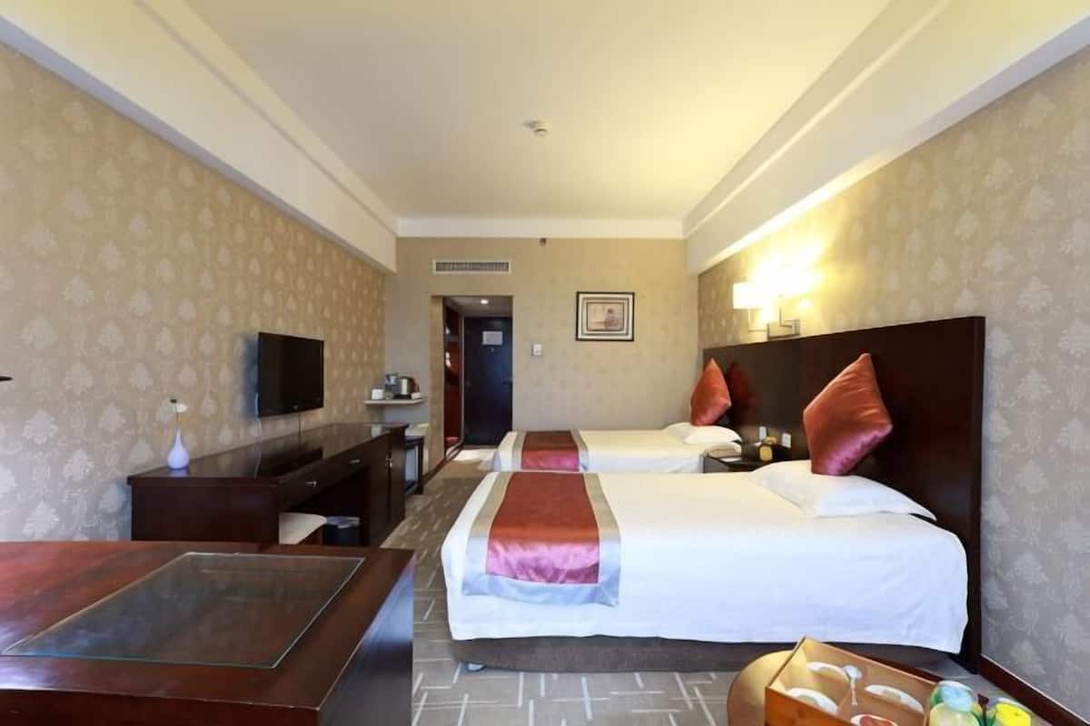 A hotel room with two beds, a desk, a television, and a minibar.