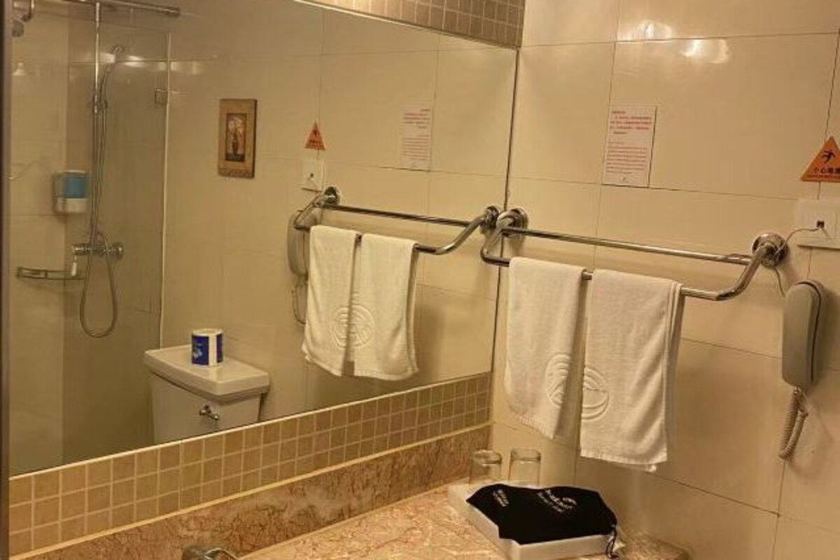 Un baño con cabina de ducha de vidrio, inodoro, toallero con varias toallas, espejo y teléfono.