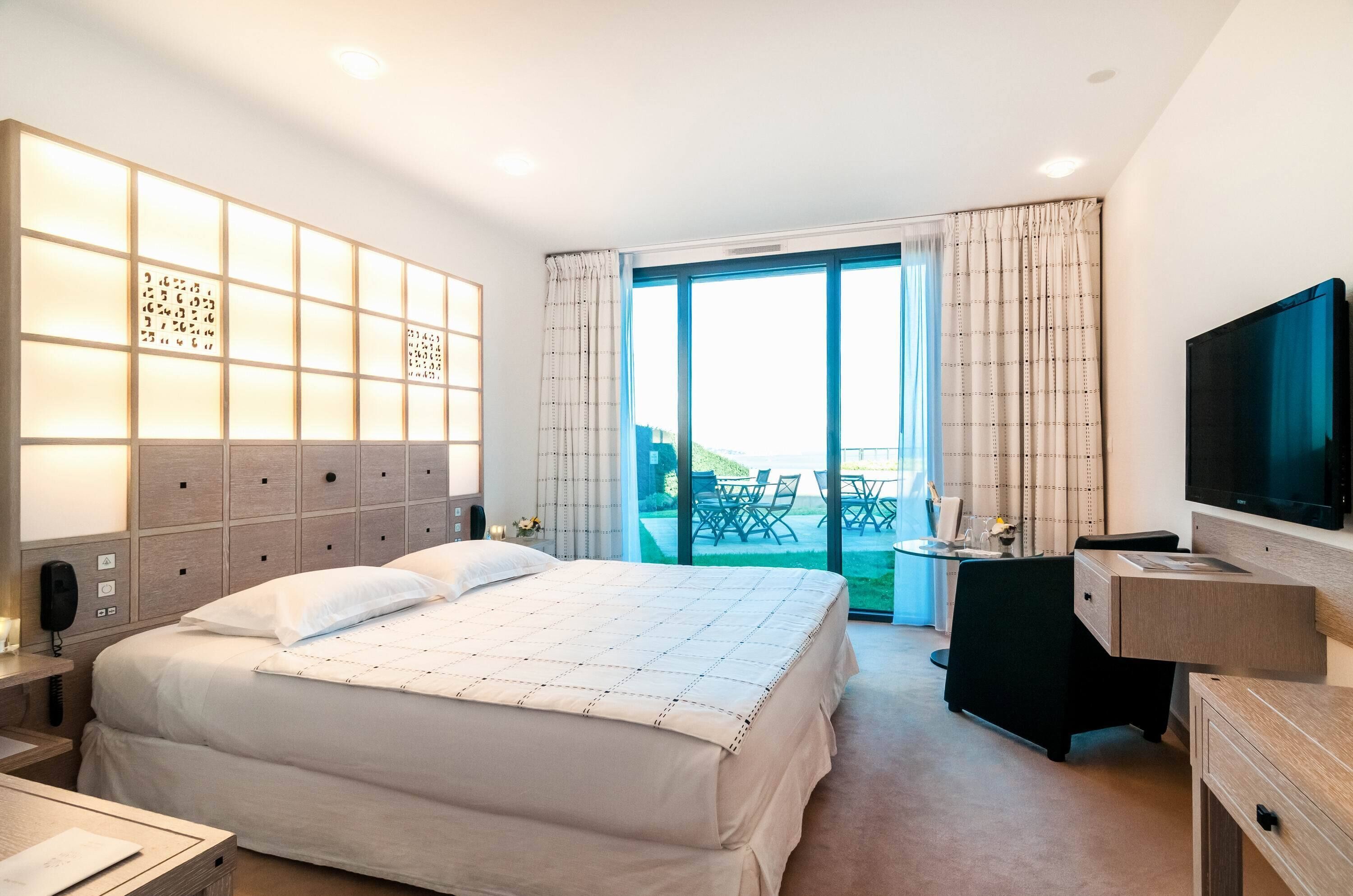 Una camera d'albergo con un letto, una scrivania, una televisione e un balcone con mobili da esterno.