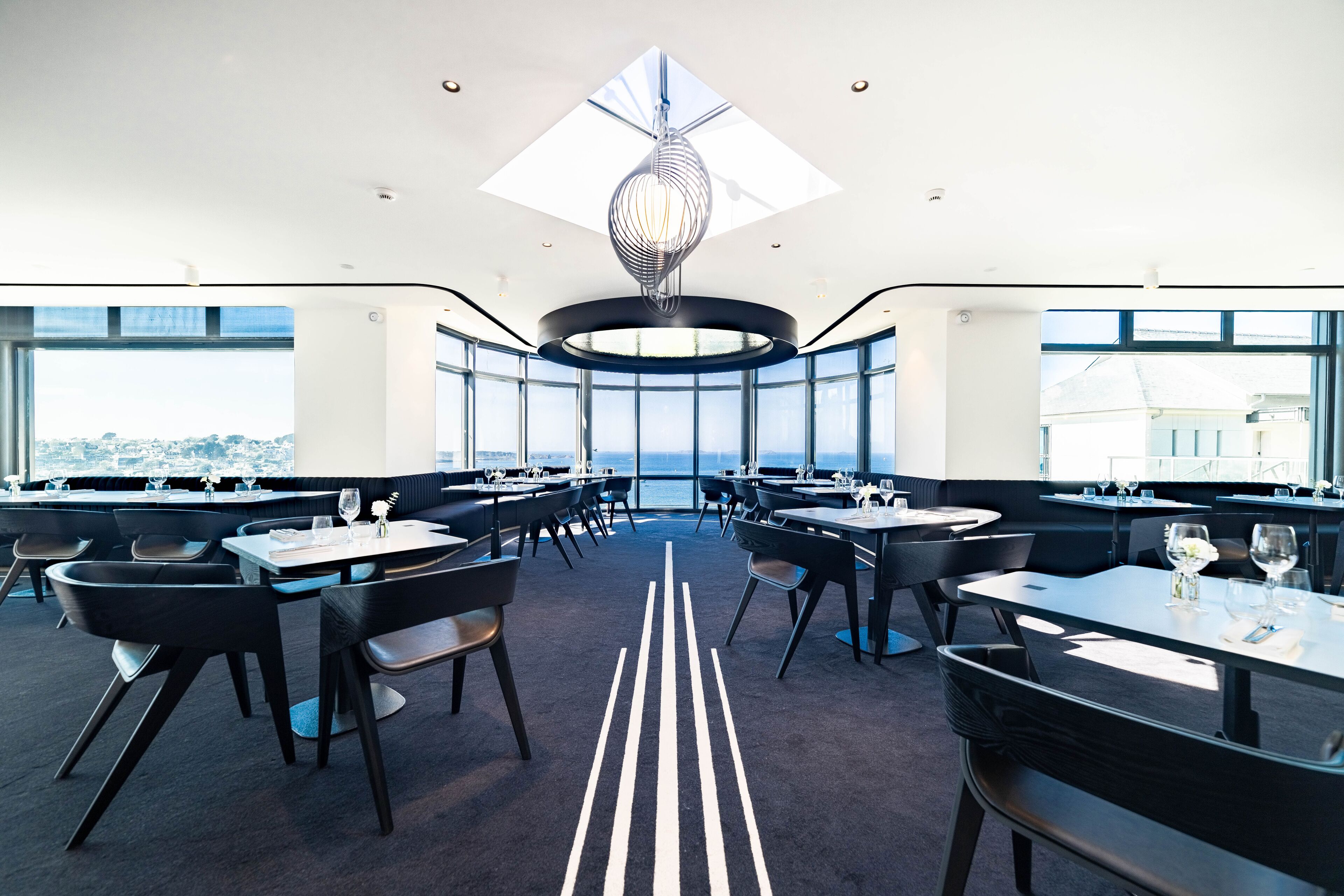 Un comedor moderno con mesas y sillas redondas, ventanas amplias que ofrecen vistas a la ciudad y una lámpara de techo original.