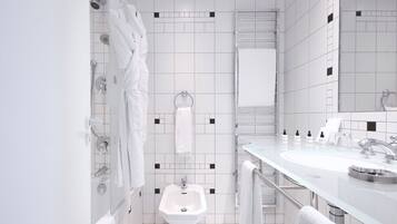 Ein modernes Badezimmer mit weißen Fliesen, einem Bidet, einem Waschbecken mit Spiegel und mehreren Handtüchern.