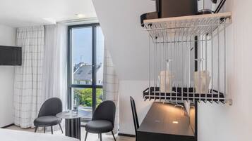 A modern hotel room with a large bed, a dining table with chairs, a built-in TV, and a window with curtains.
