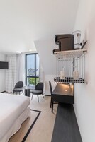 Una habitación de hotel moderna con una cama grande, una mesa de comedor con sillas, una televisión integrada y una ventana con cortinas.