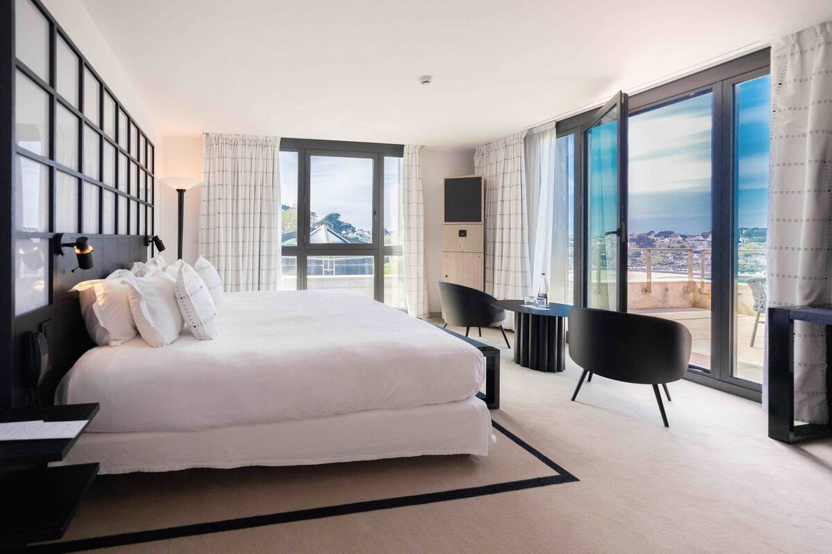 A modern hotel room with a large bed, a desk, a chair, and a TV.