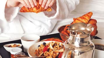 A breakfast tray with croissants, cereal, fruit, and a coffee pot.