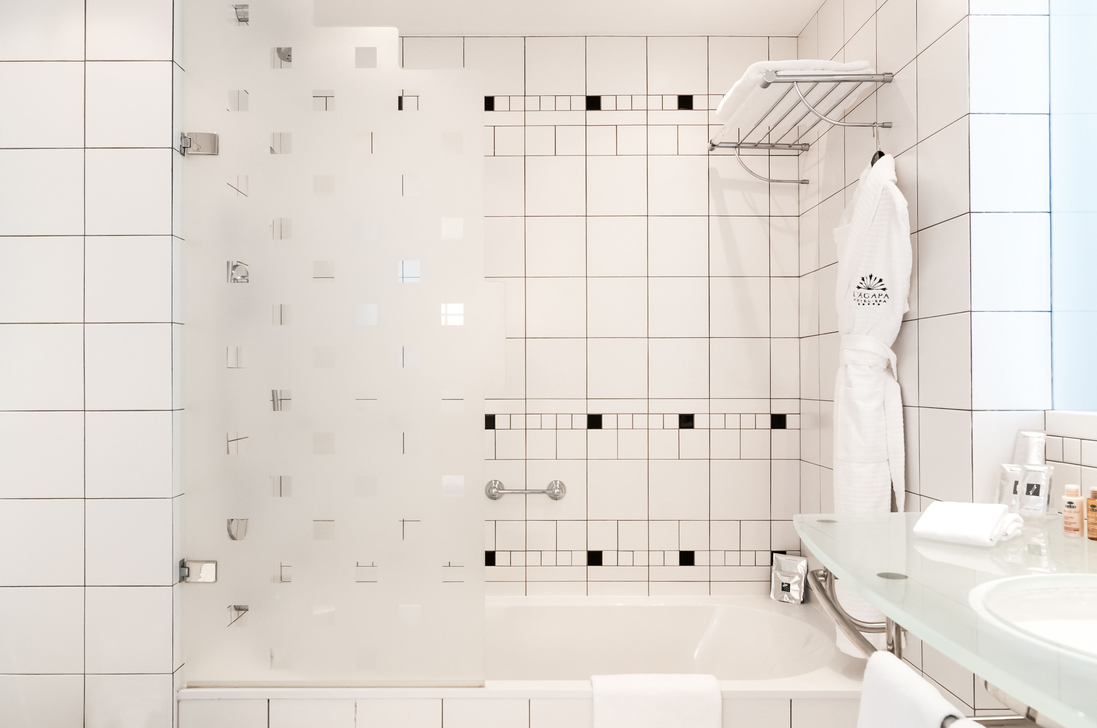 Un baño moderno con cabina de ducha de vidrio, tocador de vidrio y una toalla blanca colgada en la pared.