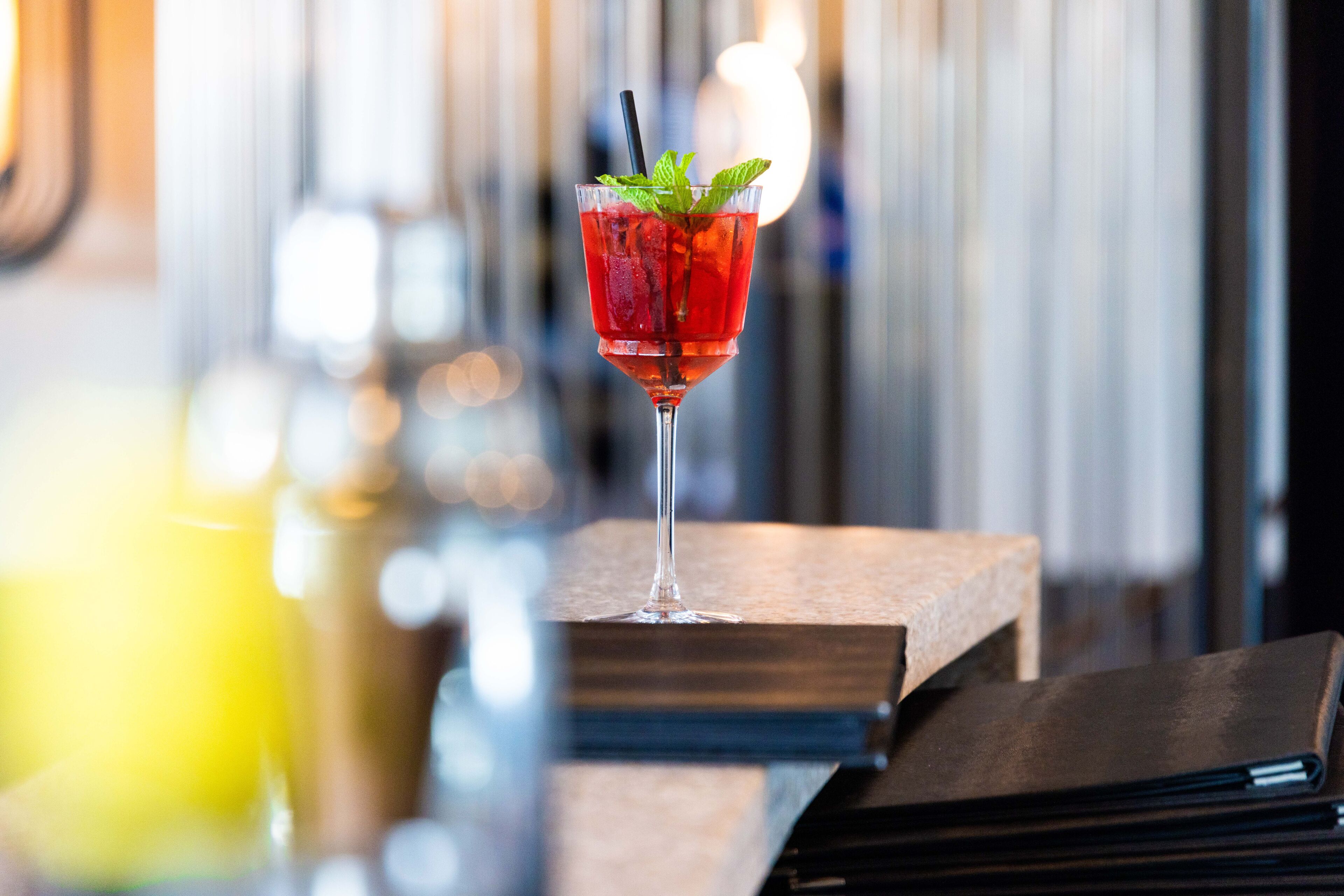 A cocktail in a glass with a straw and mint garnish on a wooden bar counter.