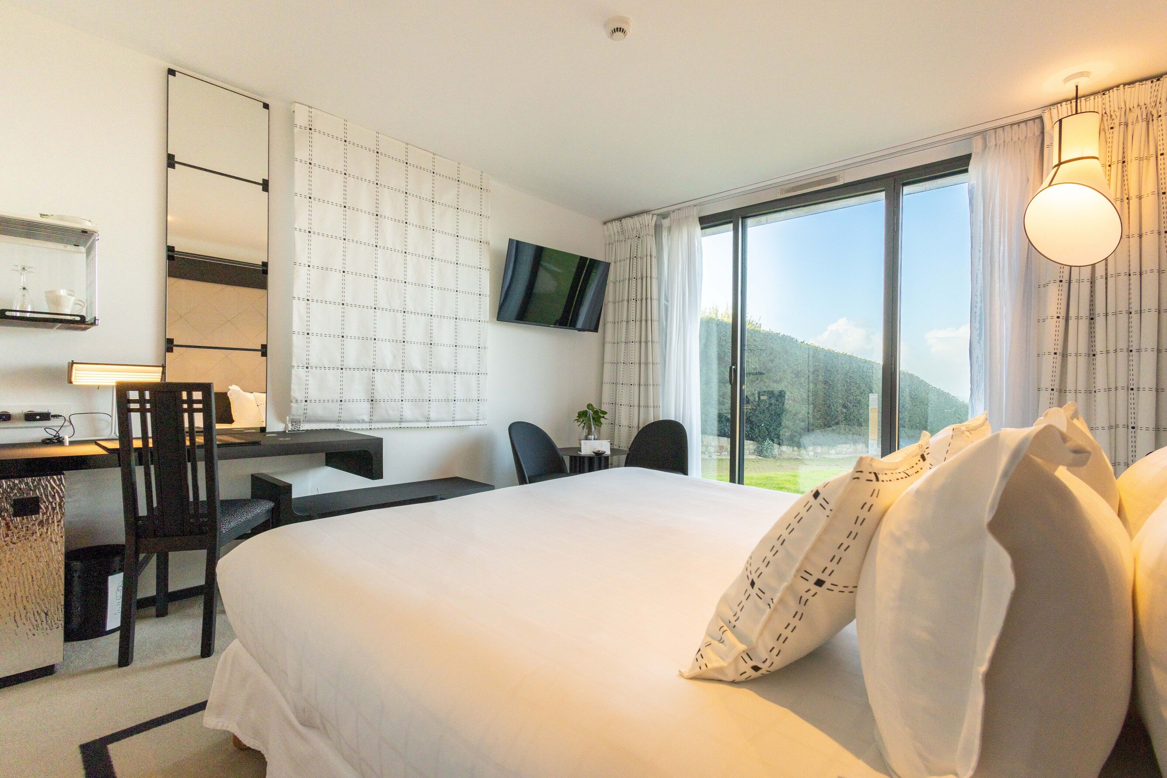 Une chambre d’hôtel avec un grand lit, un bureau avec une chaise, une télévision et une vue sur l’extérieur.