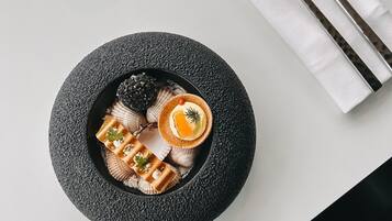 A round black plate with a dessert, a fork, a knife, and two glasses on a white table.