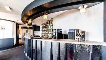 Una zona de bar moderna con una barra curva, estantes llenos de botellas y una máquina de café.
