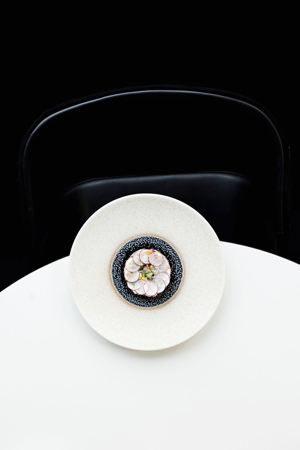 Un plato blanco con un diseño decorativo en el centro, sobre una mesa blanca frente a una silla negra.