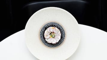 Un plato blanco con un diseño decorativo en el centro, sobre una mesa blanca frente a una silla negra.