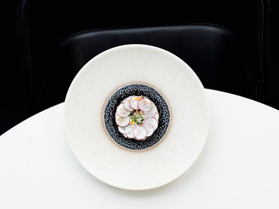 Un plato blanco con un diseño decorativo en el centro, sobre una mesa blanca frente a una silla negra.