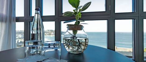 A table with a glass jar containing a plant, a bottle, and a glass of water.