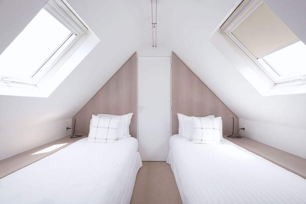 A modern, well-lit room with two beds, a skylight, and a wooden accent wall.