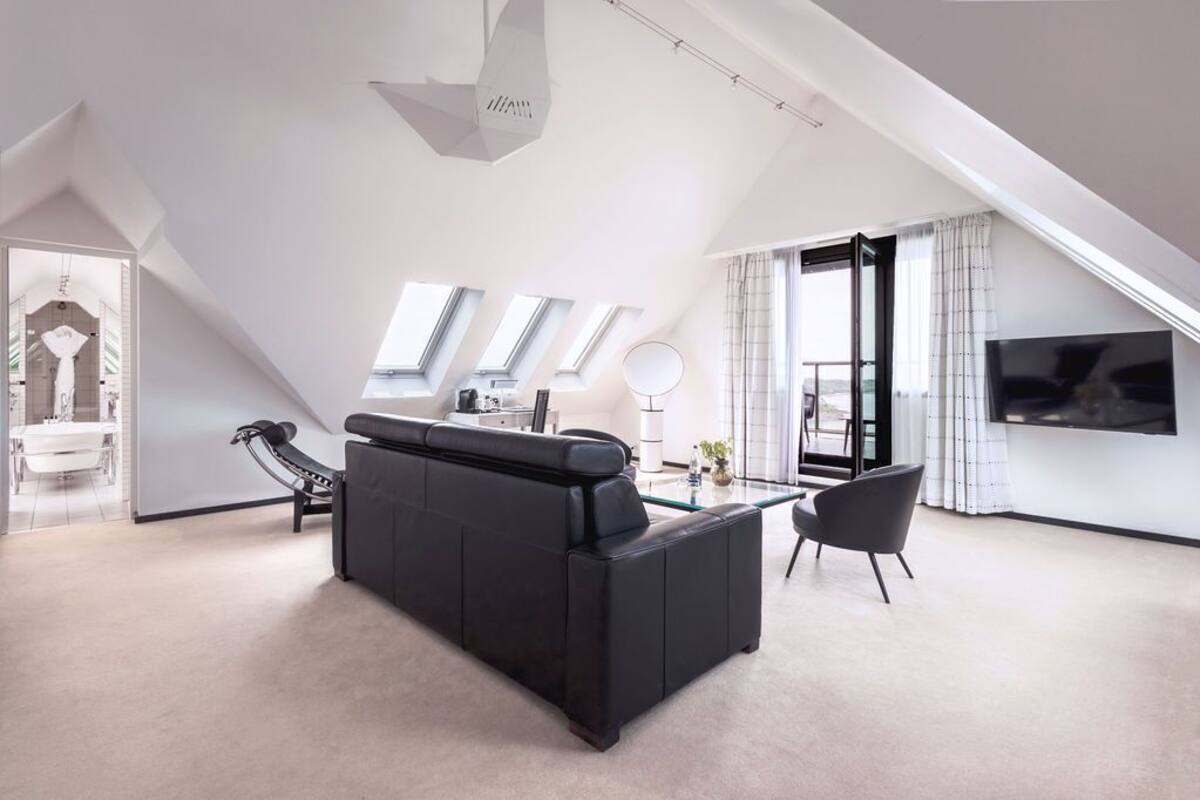 A modern living room with a black sofa, a glass coffee table, and a TV mounted on the wall.