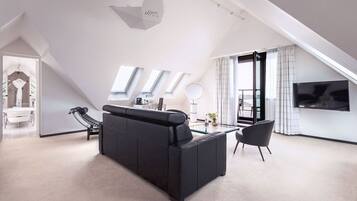 Un salon moderne avec un canapé noir, une table basse en verre et un téléviseur fixé au mur.