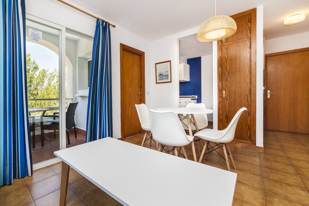 Ein modernes Zimmer mit einem weißen Tisch und Stühlen, Holztüren und Blick auf einen Außenbereich.